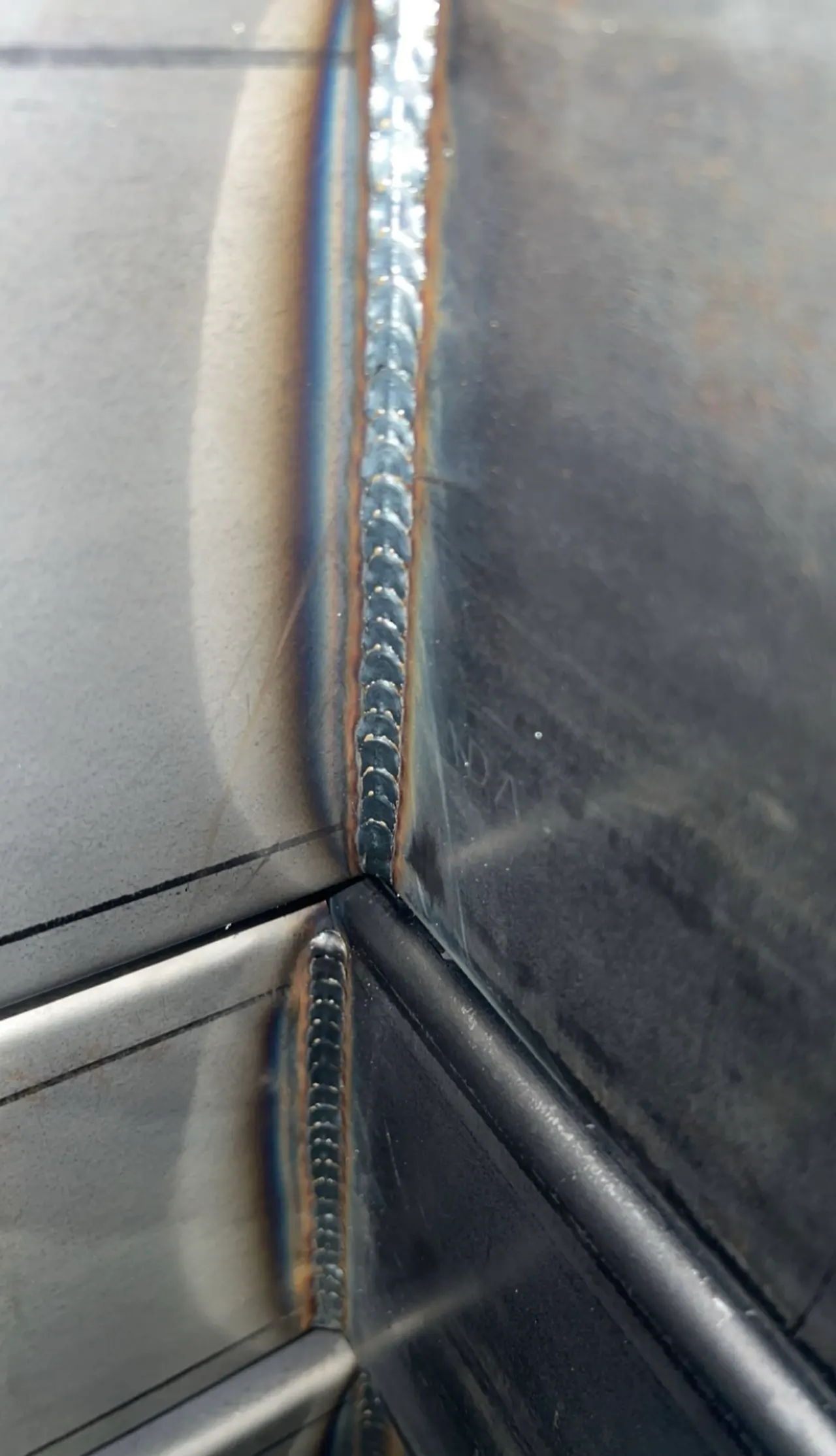 Close-up of MIG welds with a stacked-dime appearance joining metal panels