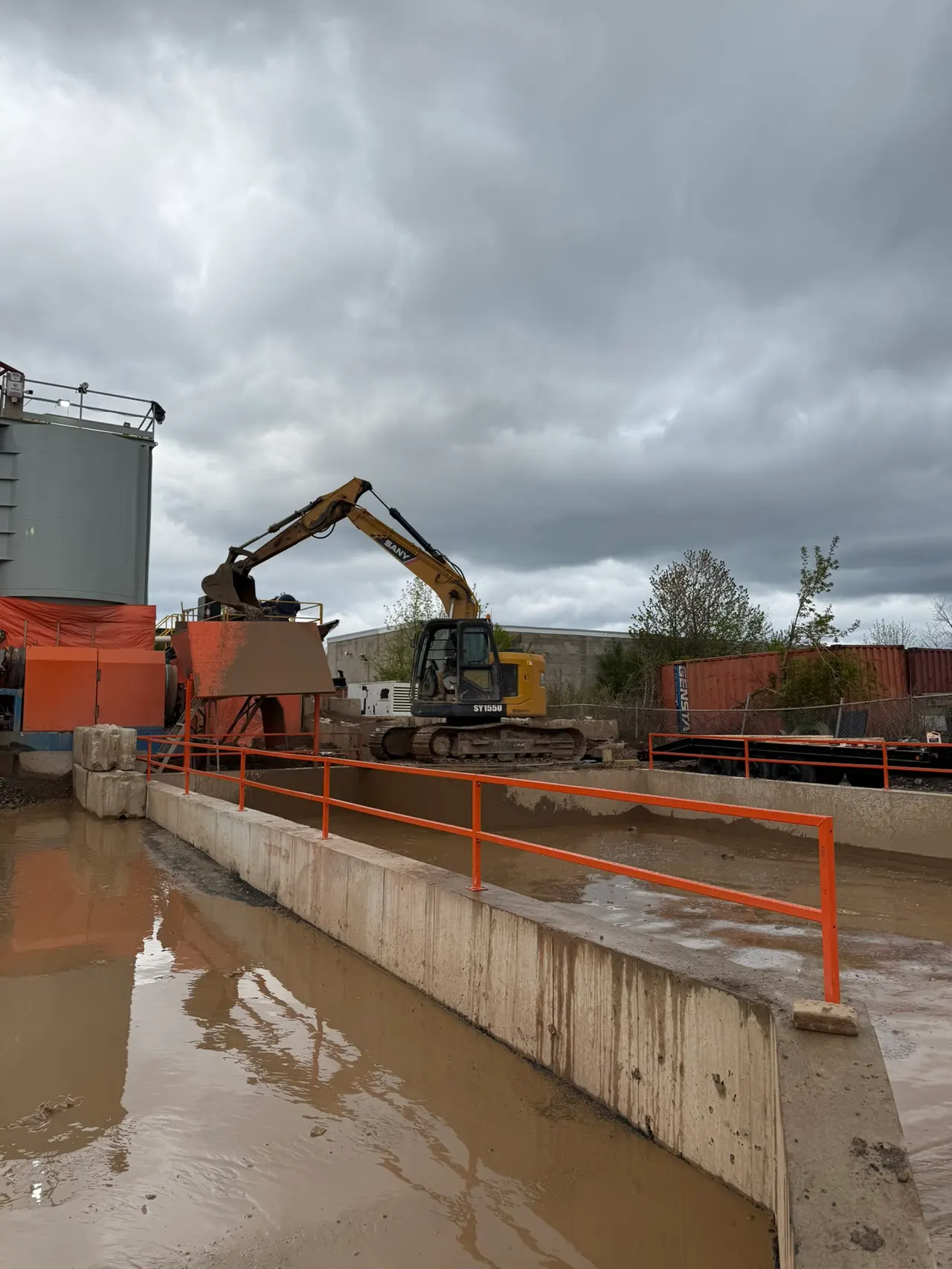 Bright orange railings alongside a concrete washout pit, with plant machinery behind